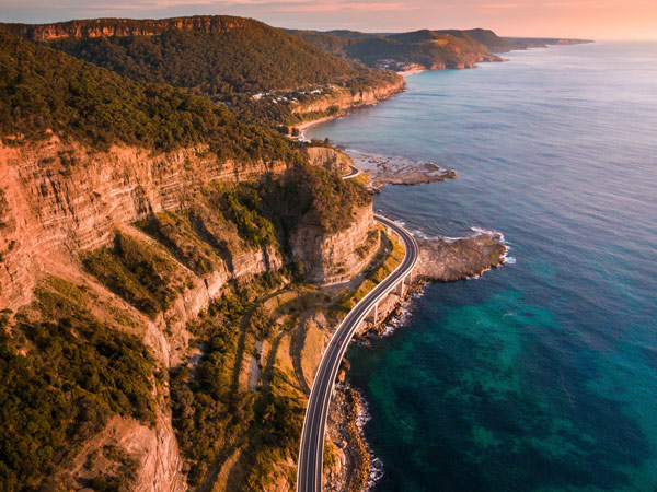 Aerial overlooking cars driving along Sea Cliff Bridge, Clifton