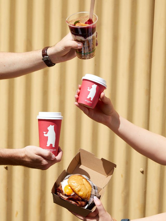 hands holding coffee cups and sandwich at Flying Bear