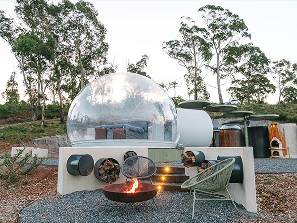 A firepit and a bubble tent in the bush.