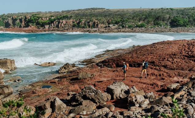 Two people walking on the rocky shoreline near the ocean. Light to Light walk