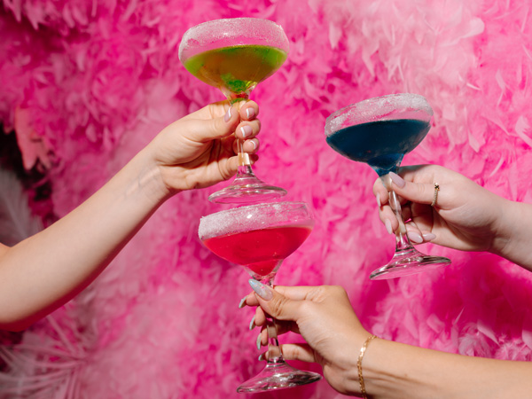 hands holding cocktail glasses on pink background