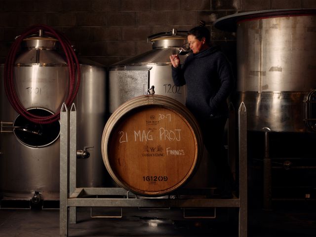 A winemaker sipping a glass of wine from a barrel