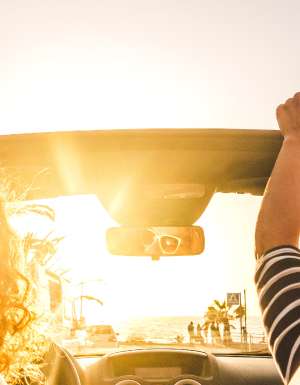 Couple of woman friends traveling and driving having a lot of fun dancing in the car with opened roof and summer vacation sunset ocean in front