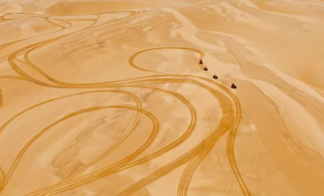 Four rugged 4WDs kick up trails of golden dust as they charge across the sweeping desert landscape.