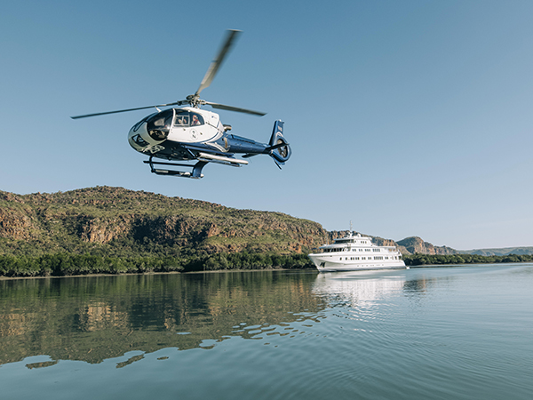 A helicopter soars above the sea, with a sleek cruise ship gliding in the distance.