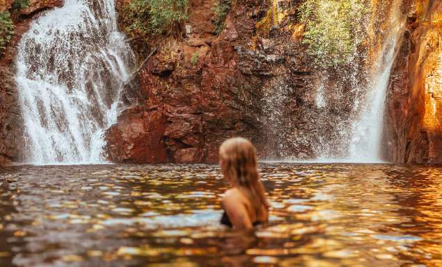 Surrounded by lush forest, a woman cools off in Florence Falls, just one of many incredible things to do in the Northern Territory.