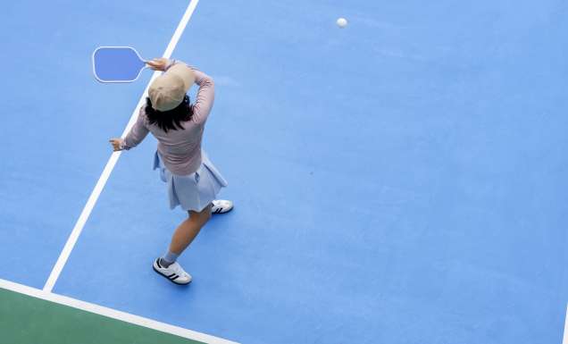 top view of woman playing pickleball, holding paddle to return ball in pickleball court