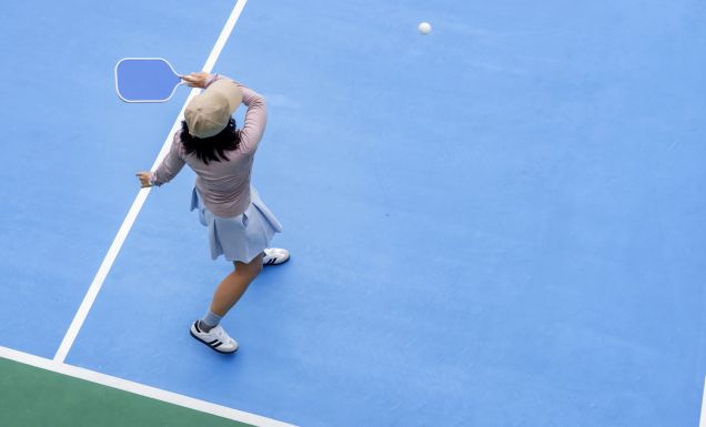 top view of woman playing pickleball, holding paddle to return ball in pickleball court