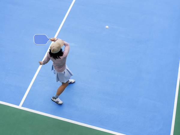 top view of woman playing piclke ball, holding paddle to return ball in pickleball court