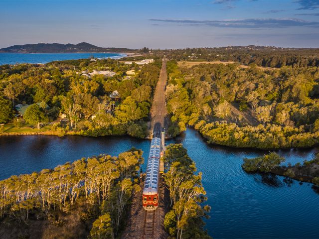 A historic red train crossing a bridge over water 
