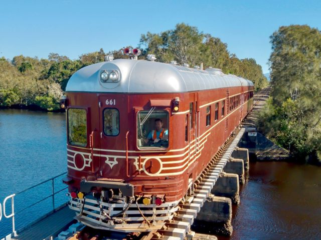 A historic red train crossing a bridge over water on a clear day
