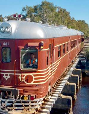 A historic red train crossing a bridge over water on a clear day