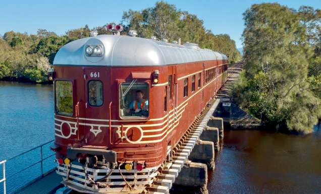 A historic red train crossing a bridge over water on a clear day
