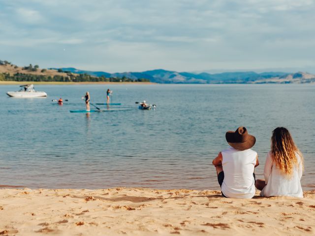 two people watching SUP boarders and a boat our on the water at lake hume