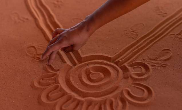 A hand maps the Mala Walk in the red sand of Uluru