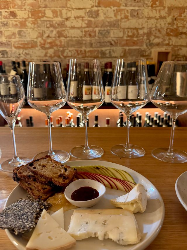 A cheese plate and wine glasses lined up in a wine cellar at The Tasman