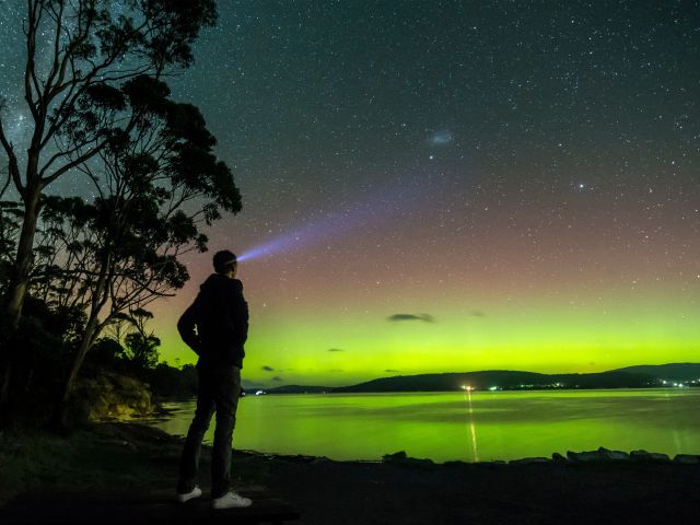 A man with a head torch looking at the Aurora Australis