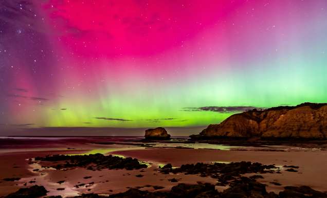 An Aurora Australis display at night along the coastline