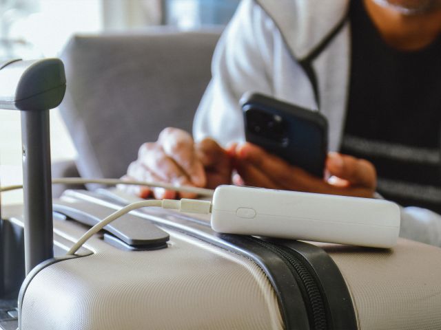 A person charging their phone from a power bank that's sitting on a suitcase