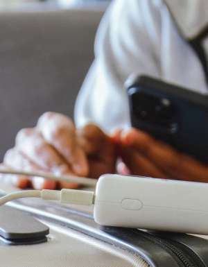A person charging their phone from a power bank that's sitting on a suitcase
