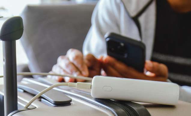 A person charging their phone from a power bank that's sitting on a suitcase