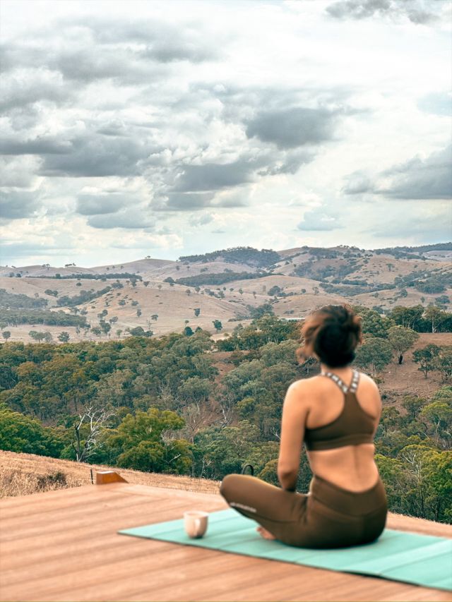 A woman sitting on a yoga mat on a deck looking at mountains