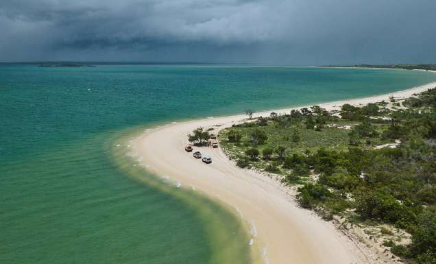 Aerial shot of East Arnhem’s coastline as cars trace the curve of the shore.