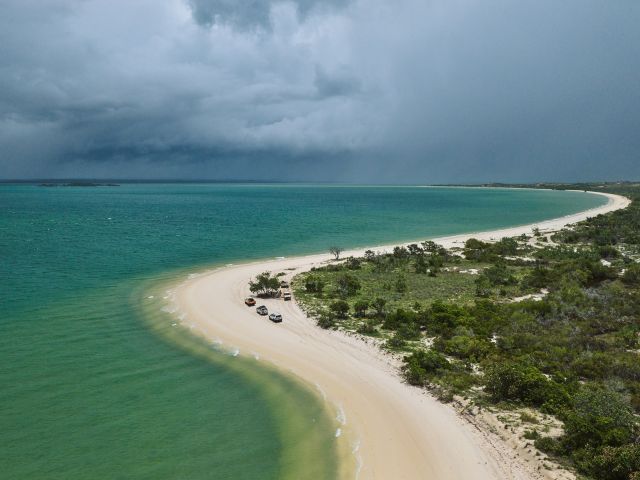 Aerial shot of East Arnhem’s coastline as cars trace the curve of the shore.