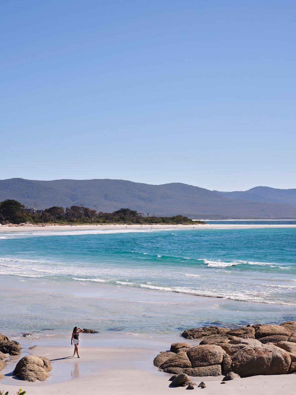 Woman walks on Waubs Beach in Bicheno