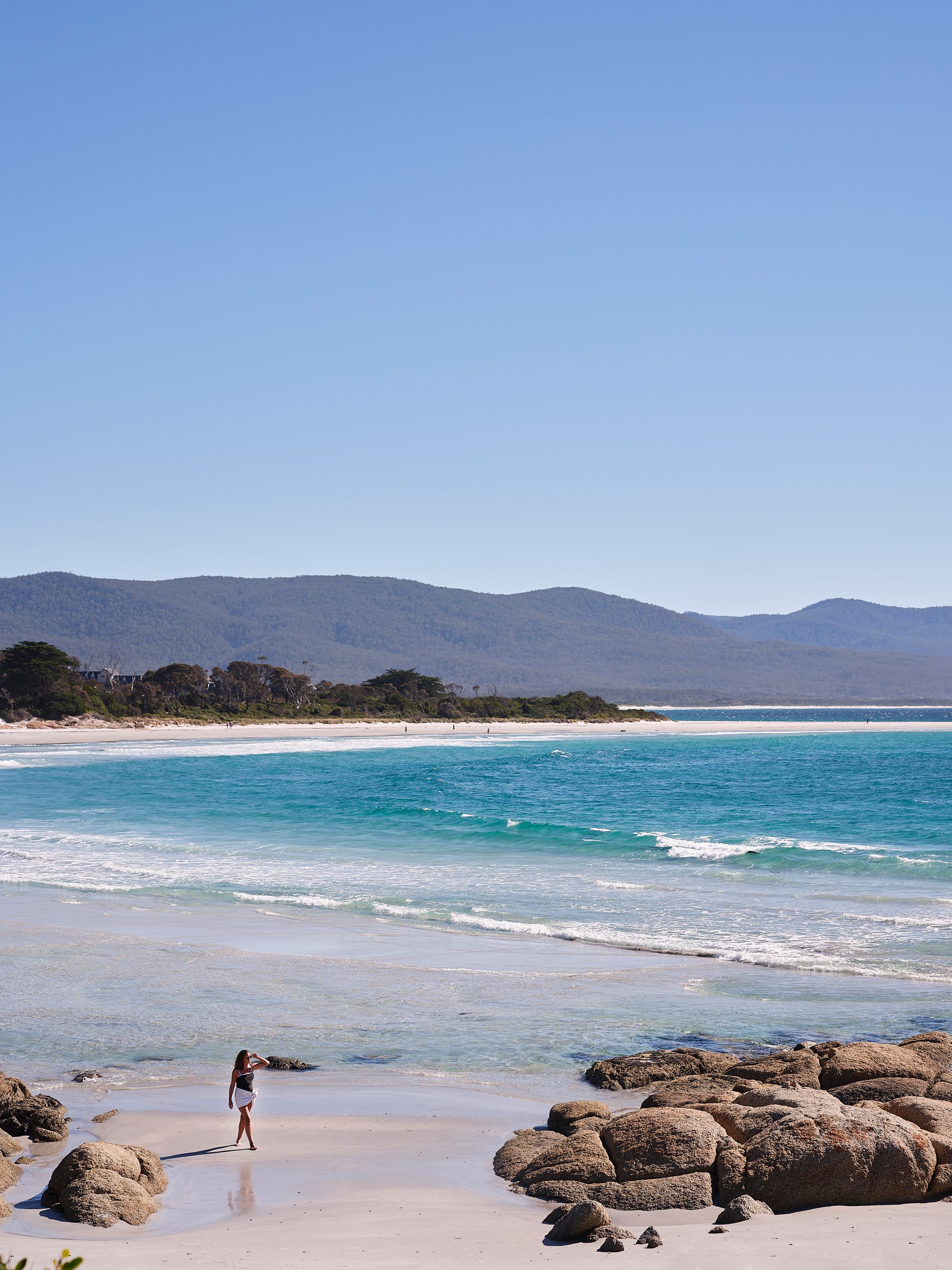 Woman walks on Waubs Beach in Bicheno
