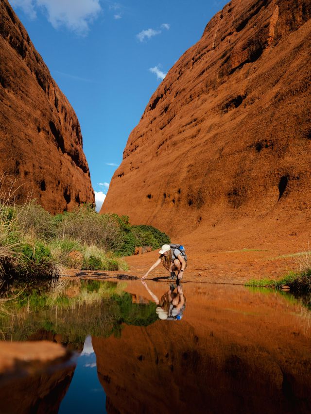 A woman reaching out to touch a natural waterhole at Kings Canyon during the best time to explore the NT.