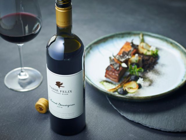 A bottle of Cabernet Sauvignon paired with a beautifully plated gourmet meal at a winery restaurant.