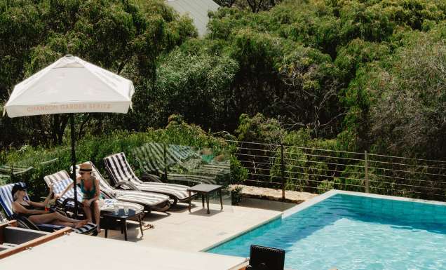 Two women enjoying drinks by the pool with ocean views.