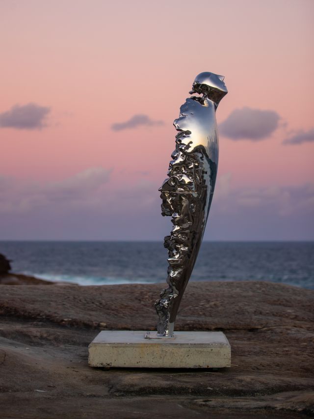 Lu Lu’s mirror-polished sculpture Ascent reflecting a pink dawn sky on the Bondi to Tamarama coastal walk
