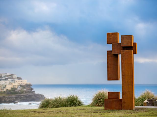 Nenad Milovanović’s rust-red block sculpture Support IV on a grassy headland at Sculpture by the Sea, Bondi