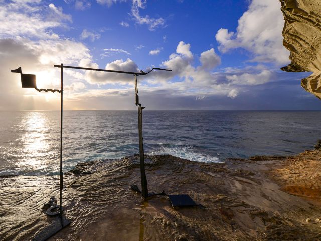 Orest Keywan’s steel sculpture Eastern Gate II on the rocks with the sun over the ocean at Sculpture by the Sea, Bondi