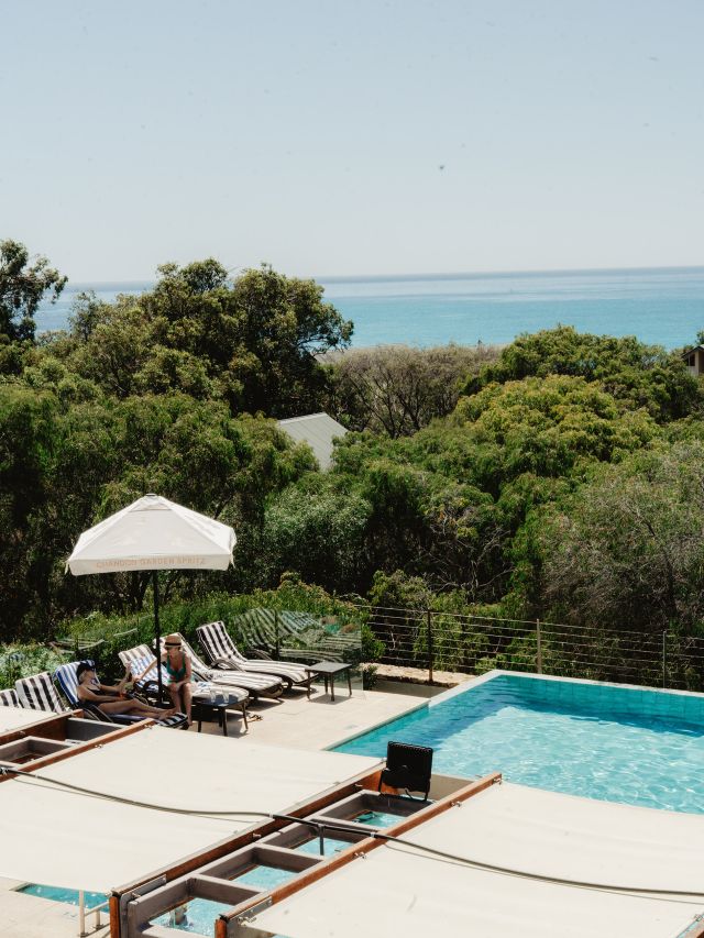 Two women enjoying drinks by the pool with ocean views.