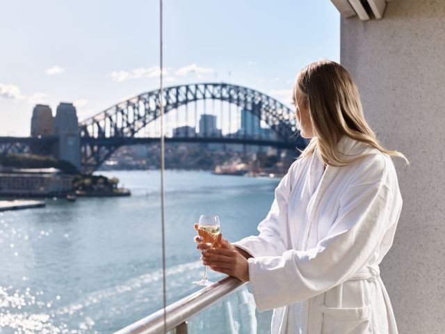A woman sipping champagne in her bathrobe while admiring Sydney Harbour Bridge.