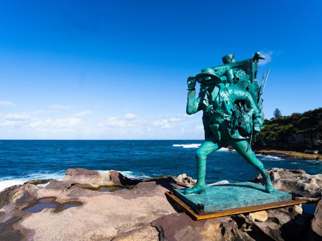 Tim Storrier’s green figurative sculpture Wayfarer on the rocks above the ocean at Sculpture by the Sea, Bondi